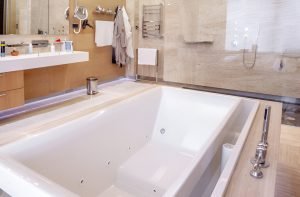 White hot tub in functional marble bathroom with mirror and walk-in shower